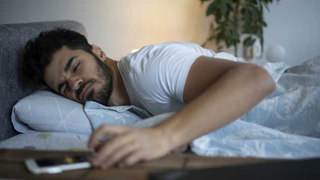 man in bed turning off phone alarm